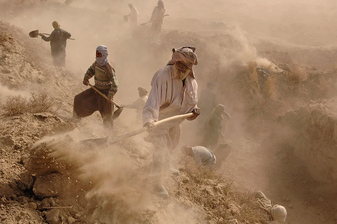 Villagers digging a canal, their figures emerging through clouds of warm dust.