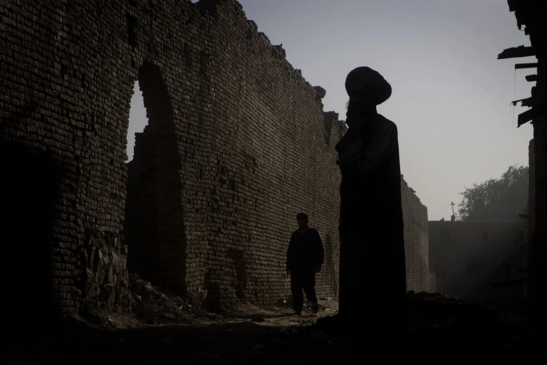 Silhouettes of people standing among tall ruined brick walls in the evening light.