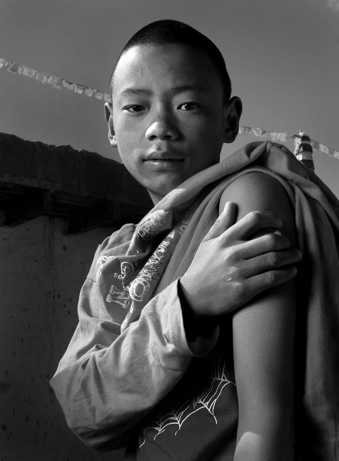 A young Buddhist monk holds his arm after receiving a vaccination, photographed in black and white.