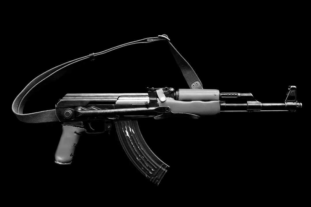 A rifle and its sling photographed in black and white against a black background.