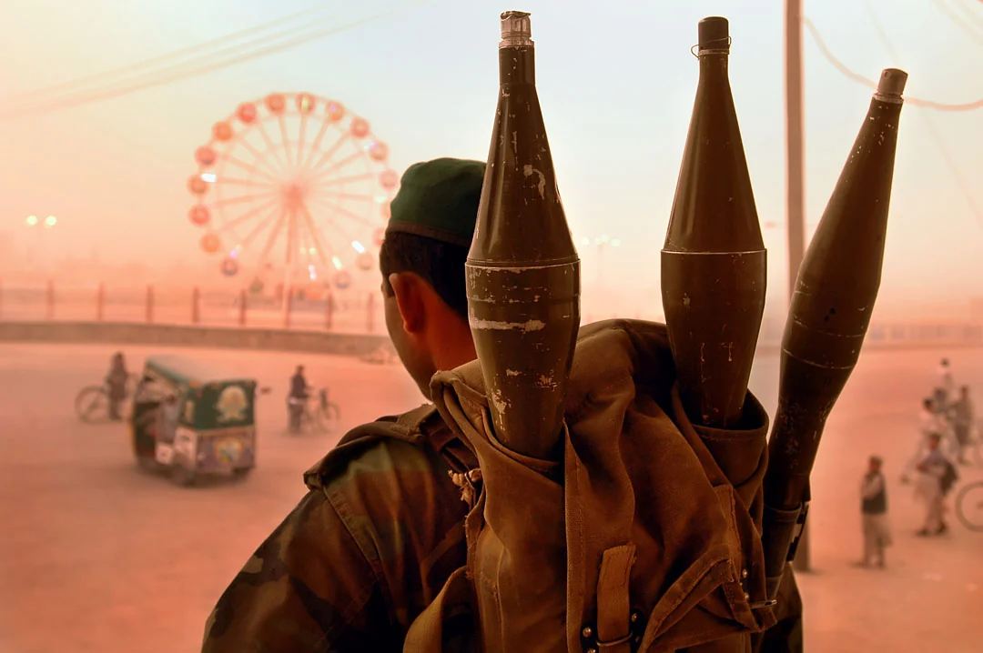 A figure carrying rocket-propelled grenades, with a fairground wheel glowing in the distance.