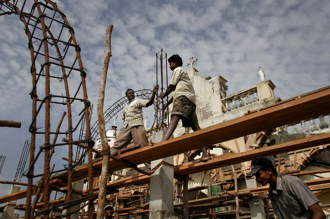 Workers rebuild a church beneath an open sky, framed by curved steel and wooden beams.